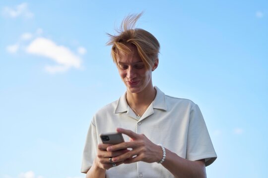 Young Man Interacts With Smartphone Under Clear Blue Sky