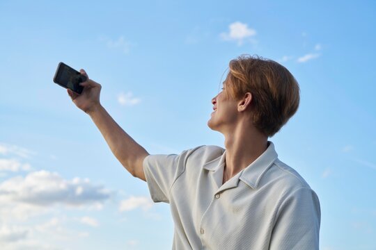 Young Person Taking a Selfie Against a Blue Sky Background
