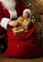 Santa Claus kneeling beside a huge red velvet sack, meticulously placing wrapped presents inside, close-up on hands adjusting ribbons and bows, golden sparkle dust in the air,
