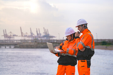 Two engineers wearing safety uniforms and hard hats communicate using a radio while reviewing data...