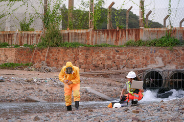 Environmental field team in protective gear analyzes water samples on a polluted beach. One holds a...