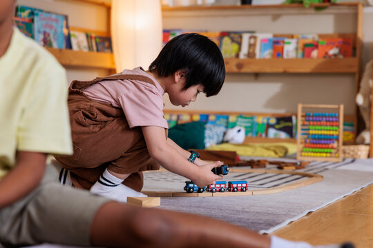 Child plays with toy train on wooden track.