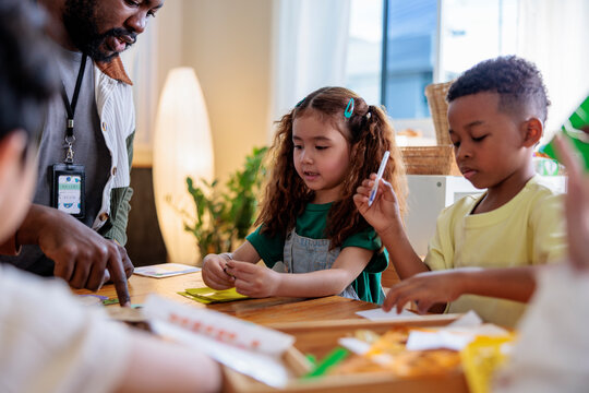 Teacher helps children with a craft project at a table.