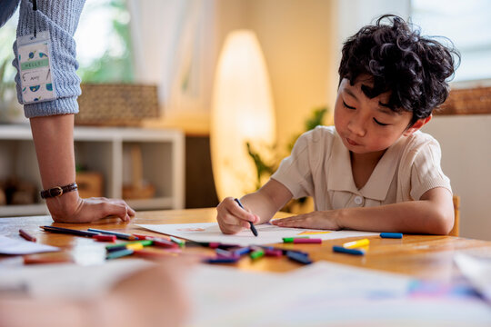 Child drawing with crayons, supervised by adult.