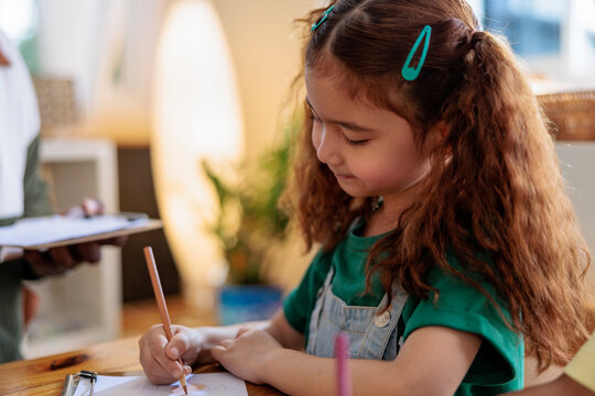 Girl with pigtails drawing on paper with a pencil.