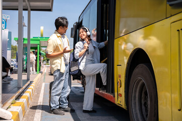 Asian tourist couple man and woman talking before going in or getting on shuttle bus at stop station