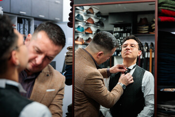 Vendor helping client with tie adjustment in clothing store