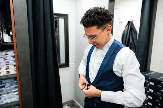 Man buttoning blue vest during fitting in store