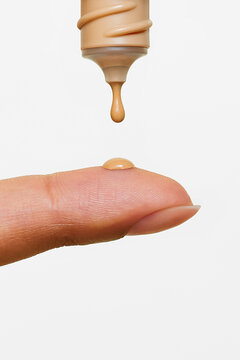 Drop of foundation falling onto fingertip against white background