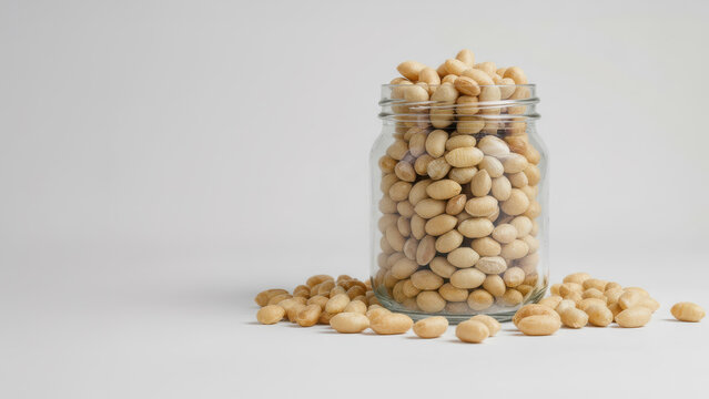 A glass jar overflowing with shelled unsalted Spanish peanuts. Tasty, healthy nuts. Mnimalist compsotion. Ample copy spacee.