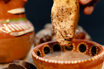 Hand dipping pan de muerto in authentic mexican chocolate