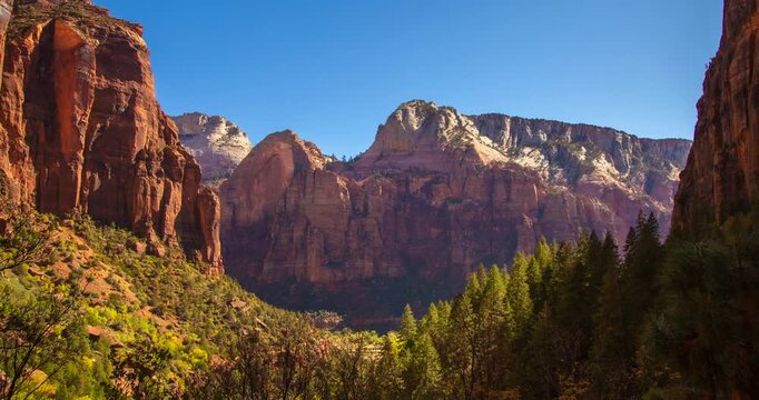 A peaceful daytime timelapse panning across the cliffs of Zion National Park, Utah. Tree shadows shift gently along the red rock walls beneath a clear blue sky, showcasing the calm landscape.
