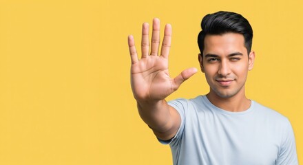 Confident young adult man winking and showing five fingers with his open palm on a vibrant yellow background, indicating stop or number five.