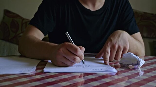 A person intently focused on writing, then crumpling and discarding a frustrated attempt.