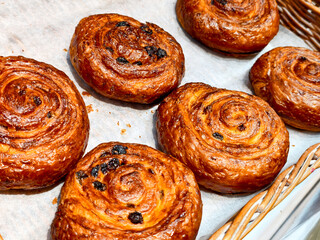 Freshly baked swirls of golden pastry with rich currants cooling on parchment paper in a cozy bakery setting