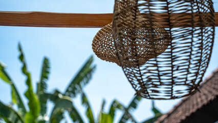 Two beautifully woven rattan or wicker light shades hang from a wooden beam, creating a natural,...