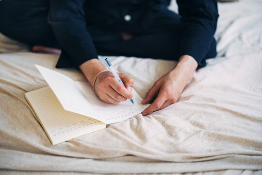 Person Writing in a Journal While Sitting on a Bed in Soft Lighting