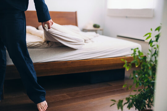 Person Making a Bed in a Cozy Sunlit Bedroom Setting