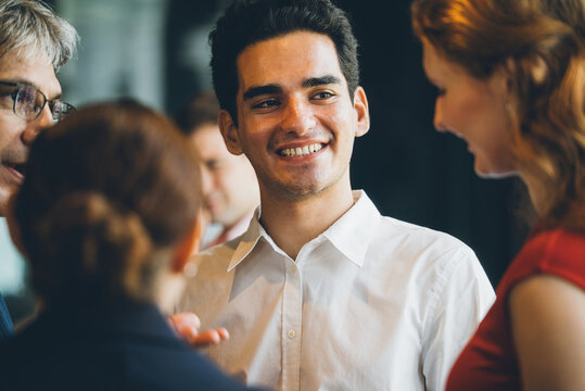 Businessman happily engaging in conversation with diverse colleagues during a corporate networking event. group is smiling and collaborating, successful professional communication, business teamwork