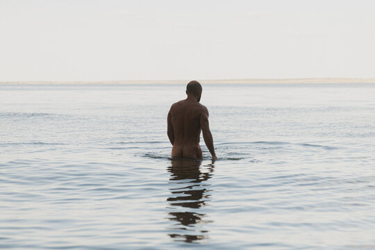 Man Wades Into Calm Water Against Serene Horizon During Twilight