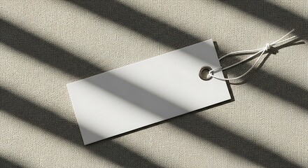 Blank white tag with string on textured fabric, casting striped shadows