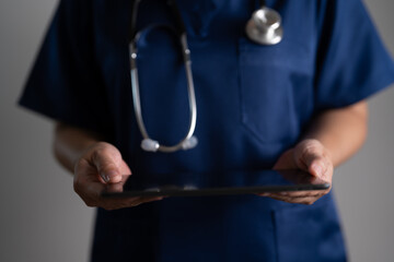 Doctor in blue scrubs holding tablet device with stethoscope, concept of telemedicine, online healthcare service, digital technology, and modern medical communication system.