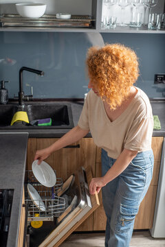 Young woman loading dishwasher with plates