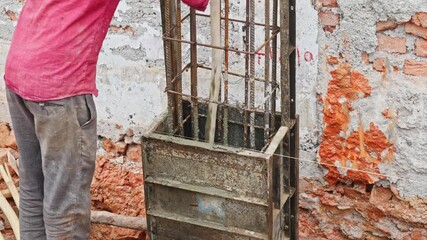 Worker levels concrete inside a steel column framework through wood stick at construction area. day time, stable shot, 4k.