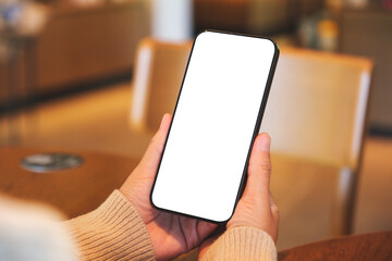 Mockup image of a woman holding and using mobile phone with blank desktop screen in cafe