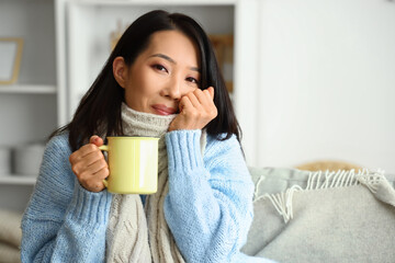 Young Asian woman with cup of hot tea at home, closeup