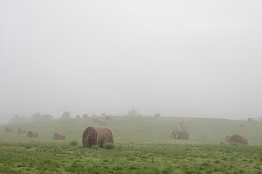 Tractor working in a green field with fog and hay bales