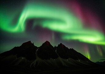 Vivid green and magenta aurora borealis dancing over dark, rugged mountain peaks at night
