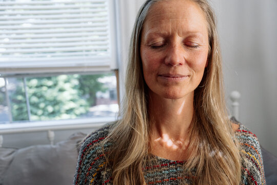 Calm woman meditating by a window, embracing peaceful serenity - Powered by Adobe