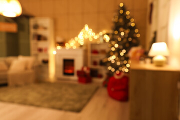 Interior of cozy living room with fireplace, shelving units and glowing Christmas tree decorated for holiday at night, blurred view