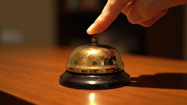 A finger presses a small gold bell on a shiny wooden surface