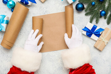 Obraz premium Santa hands with blank scroll, Christmas gifts and decorations on light background, closeup