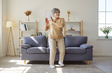 Happy senior woman dancing to music at home, enjoying leisure or weekend fun, infusing the personal...