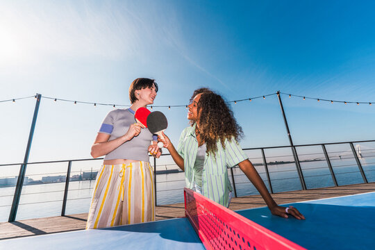 Friends playing table tennis outdoors by the water