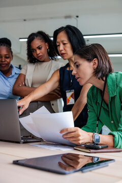 Diverse team collaborates, reviewing documents and laptop screen.
