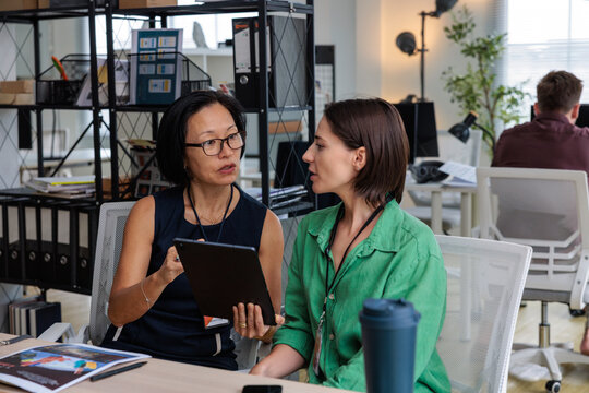 Two women discuss work using a tablet in office.