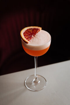 Foamy citrus cocktail with blood orange garnish in a stemmed glass