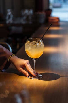Hand holding iced cocktail with straw at bar counter