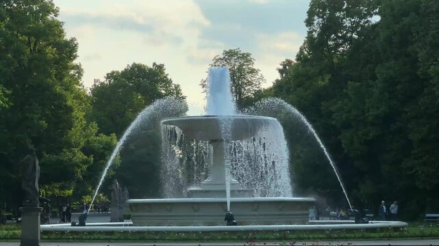 Warsaw, Poland - September 03, 2025: Majestic fountain in city park with flowing water, surrounded by lush greenery, camera pans to capture the serene atmosphere and vibrant scene