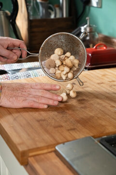 Mushrooms dropped from a strainer over a wooden cutting board