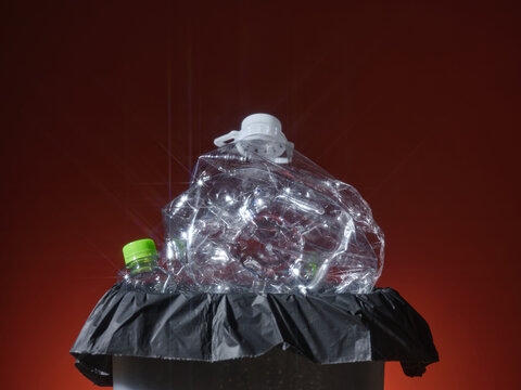 Crushed plastic bottle sitting on a trash bag against dark background