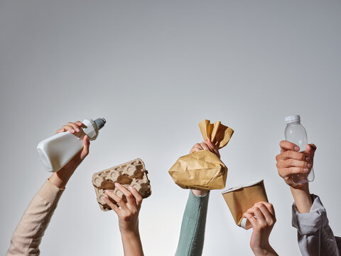 Hands holding various recyclable items against a gray background.