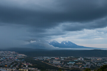 Evening urban landscape. Top view of the buildings and streets of the city. Volcanoes in the distance. Overcast weather. Low clouds. City of Petropavlovsk-Kamchatsky, Kamchatka Krai, Russian Far East.