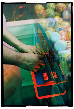 Hands Playing a Claw Machine at an Arcade
