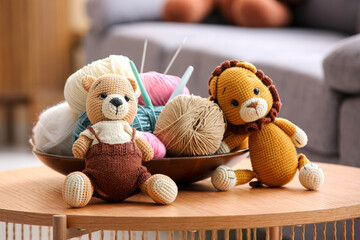 Knitted toys with yarn, knitting needles and crochet hooks on table at home