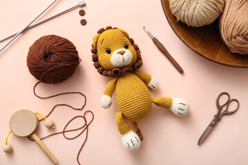 Knitted lion toy with yarn and knitting tools on beige background
